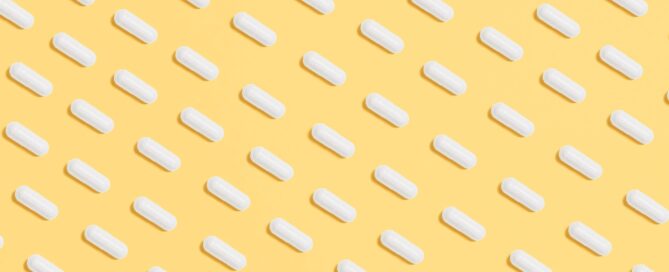 Weiße Kapseln auf gelbem Hintergrund - Symbol für Selbstmedikation bei prämenstruellen Symptomen